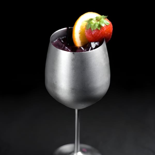 A Perico Ripiao Latin Food cocktail in a silver goblet, garnished with an orange slice and strawberry.