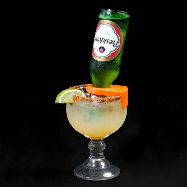 A Presidente beer bottle inverted into a large margarita glass with a lime wedge and chili salt rim.