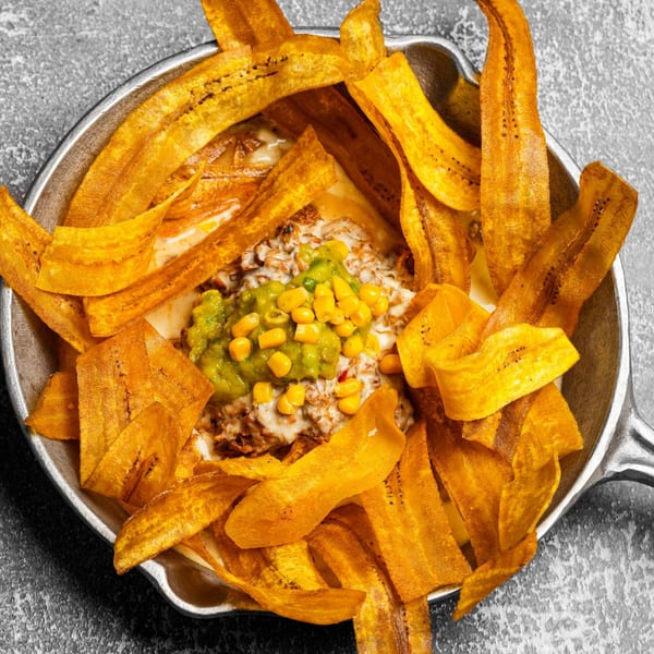 Dominican dish with crispy plantain strips surrounding a creamy dip topped with guacamole and corn.