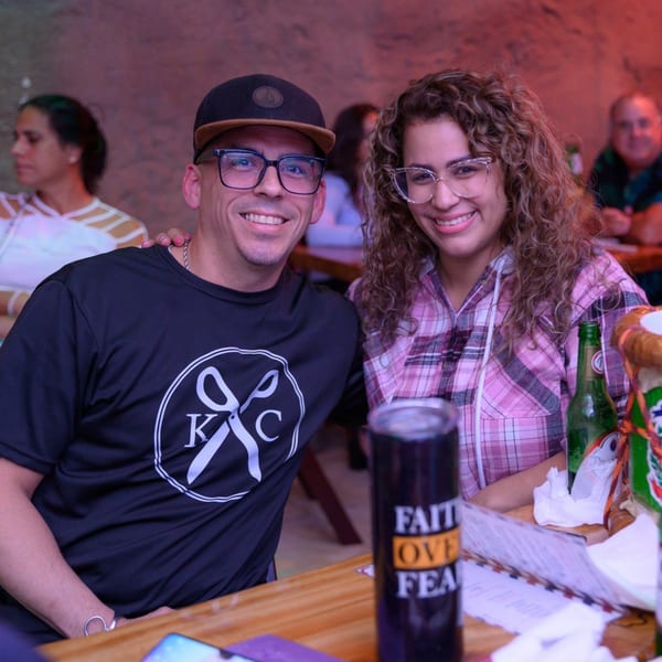 Smiling man in a cap and woman in glasses sitting at a table with drinks at Perico Ripiao.