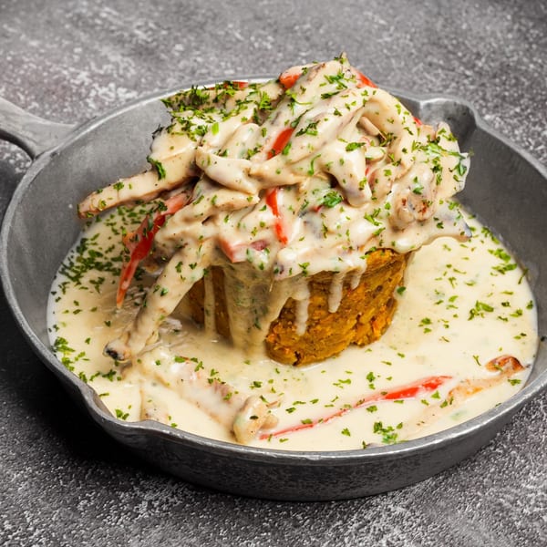 Mofongo with creamy chicken and red peppers, garnished with parsley, served in a cast iron skillet.