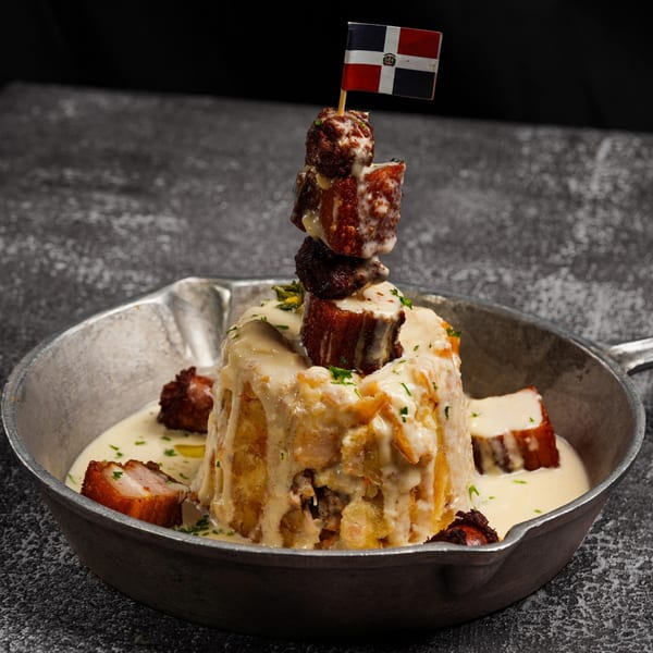 Mofongo with crispy pork belly and a Dominican flag toothpick in a metal skillet.