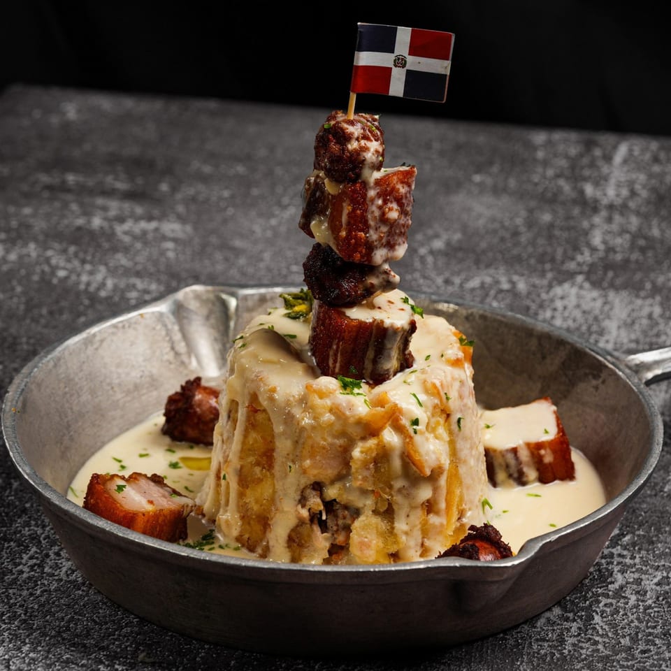 Mofongo with crispy pork belly and a Dominican flag toothpick in a metal skillet.