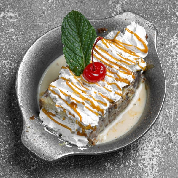 Dominican dessert with whipped cream, caramel drizzle, a cherry, and mint in a metal dish.