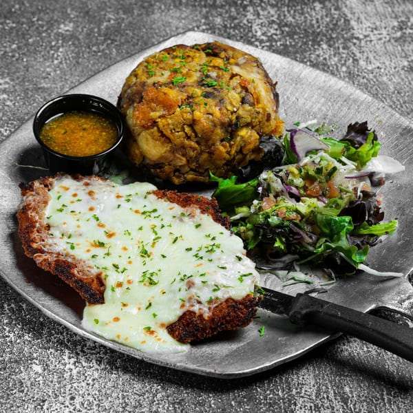 Dominican mofongo, cheesy fried chicken, side salad, and dipping sauce on a silver plate.
