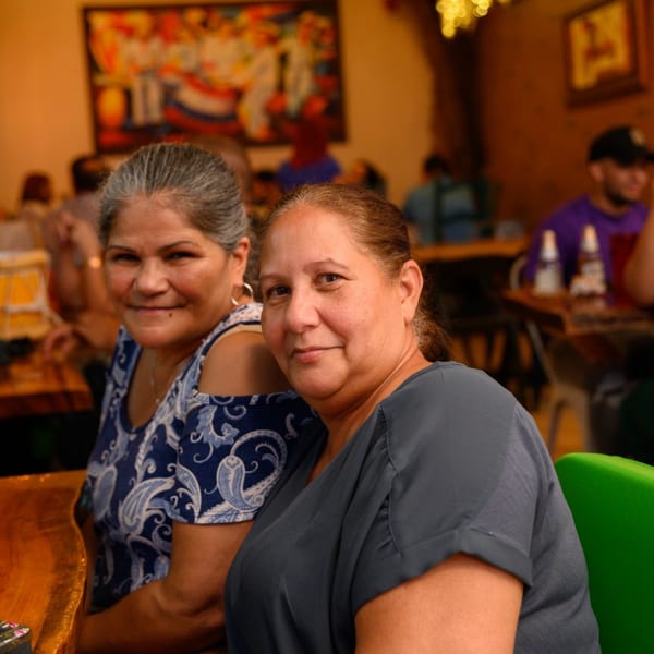Two women smiling at the camera, seated at a wooden table in a lively Dominican restaurant.